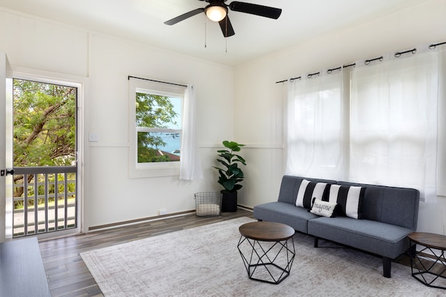 living area with ceiling fan, wood finished floors, a wealth of natural light, and crown molding