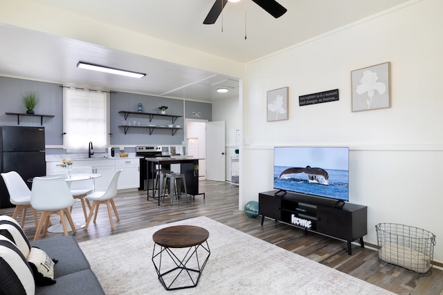 living area featuring ornamental molding, dark wood-type flooring, and a ceiling fan