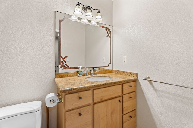 bathroom featuring a textured wall, vanity, and toilet