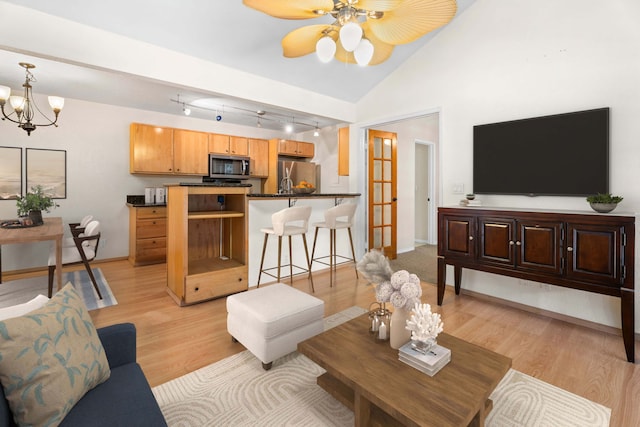 living room featuring light wood finished floors, baseboards, vaulted ceiling, and ceiling fan with notable chandelier