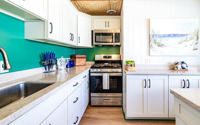 kitchen featuring white cabinets, appliances with stainless steel finishes, light stone countertops, light wood-style floors, and a sink