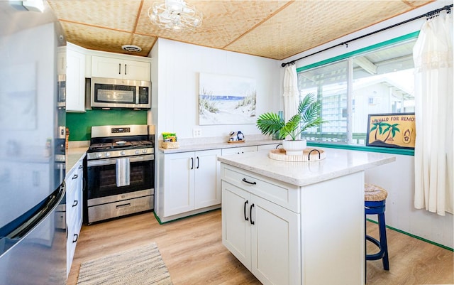 kitchen with appliances with stainless steel finishes, white cabinetry, light wood-style floors, and a kitchen bar