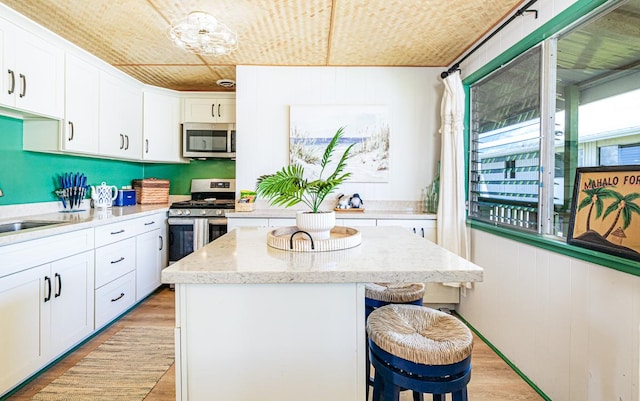 kitchen featuring a center island, stainless steel appliances, light wood-style floors, a kitchen bar, and white cabinetry