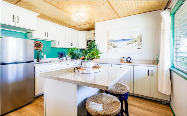 kitchen featuring stainless steel appliances, a sink, white cabinets, light wood-type flooring, and a center island