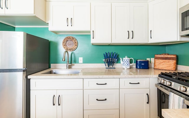 kitchen featuring stainless steel appliances, white cabinetry, a sink, and light stone counters