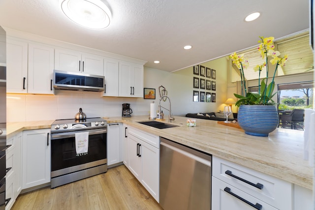 kitchen featuring white cabinets, a sink, stainless steel appliances, light wood-style floors, and backsplash