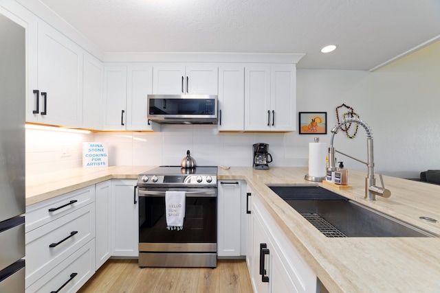 kitchen featuring decorative backsplash, white cabinets, appliances with stainless steel finishes, light wood-type flooring, and a sink