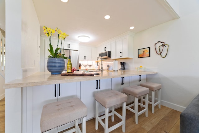 kitchen featuring light wood-style floors, refrigerator, stainless steel microwave, and a peninsula