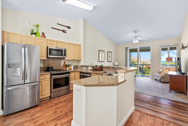 kitchen with light brown cabinets, a peninsula, light wood-style flooring, a sink, and stainless steel appliances