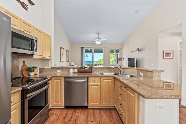 kitchen featuring wood finished floors, a peninsula, a sink, light brown cabinetry, and stainless steel appliances