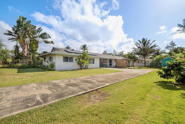 ranch-style house with roof mounted solar panels, a front lawn, driveway, and fence