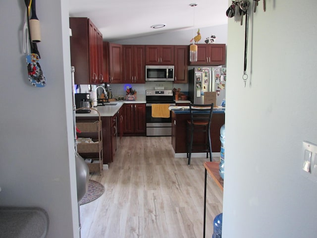 kitchen featuring stainless steel appliances, light countertops, light wood-style flooring, vaulted ceiling, and a sink