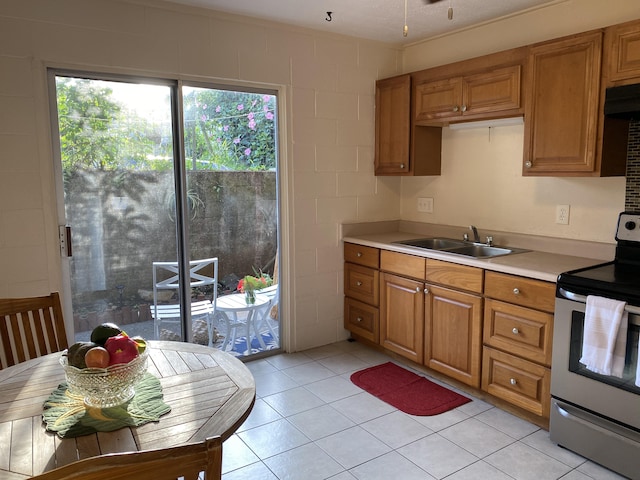 kitchen featuring brown cabinets, stainless steel electric range oven, light tile patterned floors, light countertops, and a sink