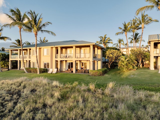 back of property with metal roof, a balcony, a lawn, and stucco siding