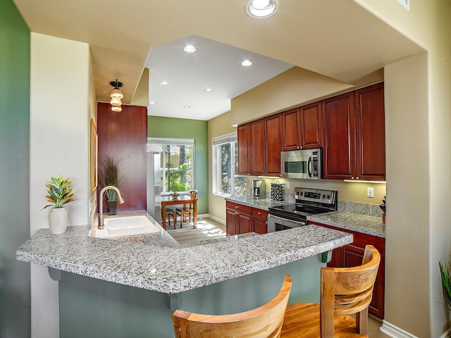 kitchen with a breakfast bar, a peninsula, recessed lighting, a sink, and stainless steel appliances