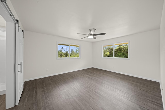 unfurnished bedroom featuring dark wood-style floors, a barn door, multiple windows, and baseboards