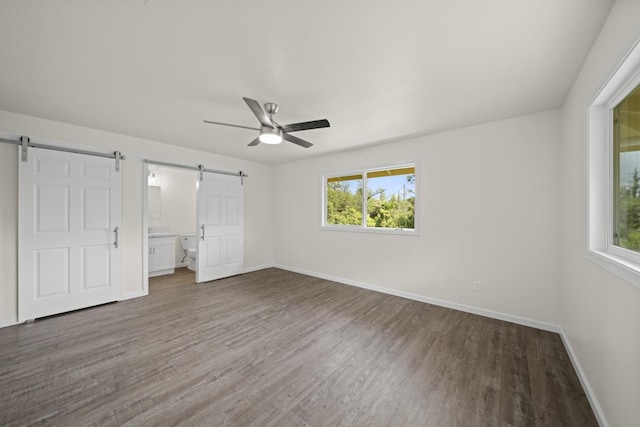 unfurnished bedroom with a barn door, dark wood finished floors, and baseboards