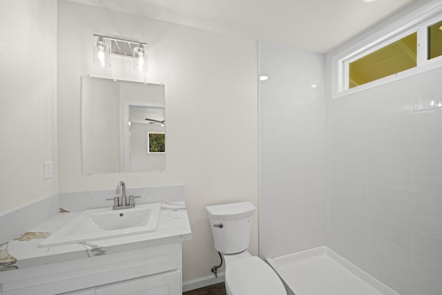 bathroom with a wealth of natural light, a tile shower, vanity, and toilet