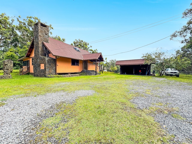 exterior space featuring metal roof, driveway, a yard, and a chimney