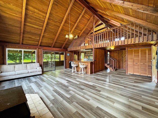 unfurnished living room with wooden walls, wood ceiling, stairway, wood finished floors, and beam ceiling