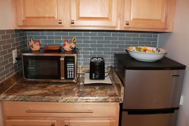 room details with light brown cabinetry, backsplash, stainless steel appliances, and dark stone counters