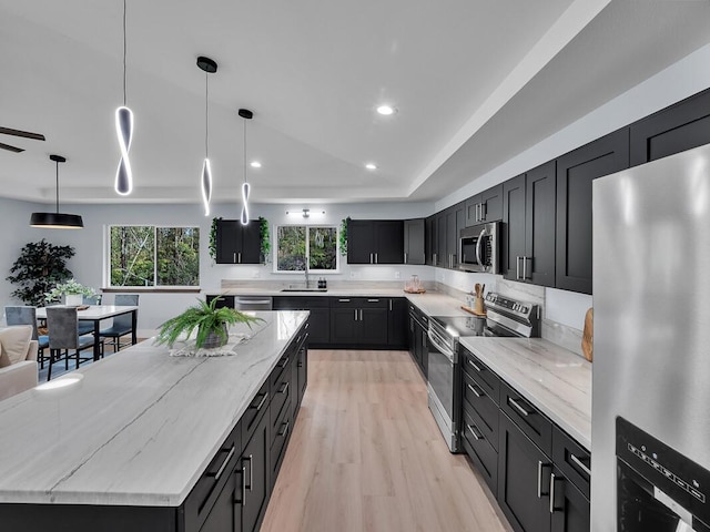 kitchen featuring light wood finished floors, light stone counters, stainless steel appliances, dark cabinetry, and a sink