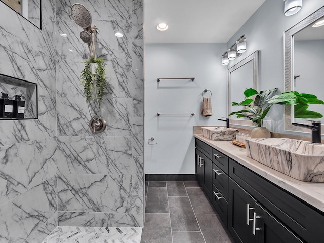 bathroom with baseboards, a sink, a marble finish shower, and double vanity