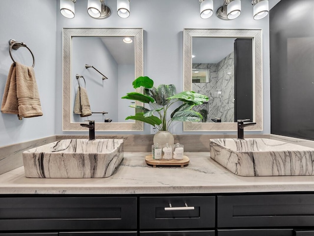 bathroom with double vanity, a marble finish shower, and a sink