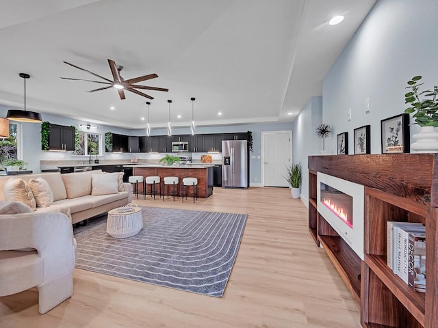 living area featuring recessed lighting, a glass covered fireplace, a ceiling fan, and light wood-style floors