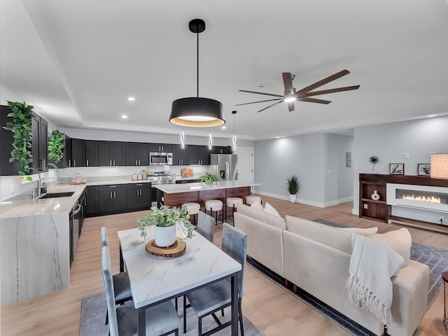 dining area with ceiling fan, light wood-style flooring, recessed lighting, baseboards, and a glass covered fireplace