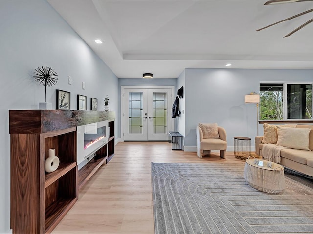 living room with light wood-style floors, a glass covered fireplace, french doors, and baseboards