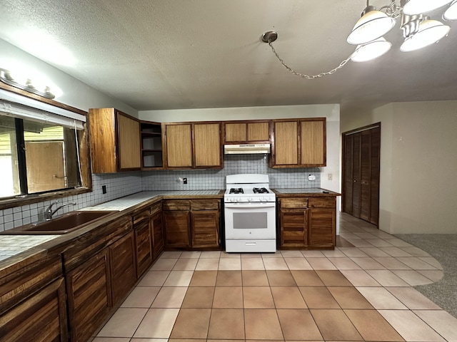 kitchen featuring under cabinet range hood, white range with gas cooktop, brown cabinetry, and a sink