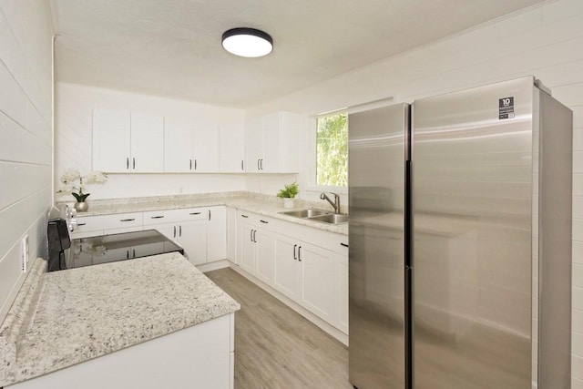 kitchen with a sink, light wood-type flooring, freestanding refrigerator, white cabinetry, and range