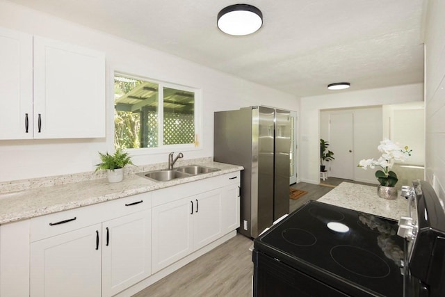 kitchen with light wood-type flooring, a sink, light stone counters, black / electric stove, and white cabinets