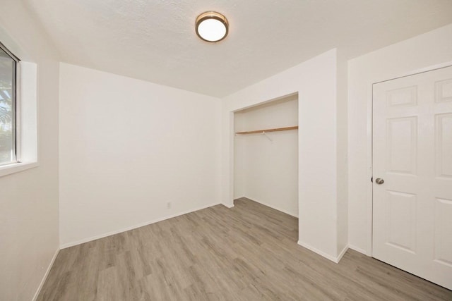 unfurnished bedroom with a closet, a textured ceiling, baseboards, and wood finished floors