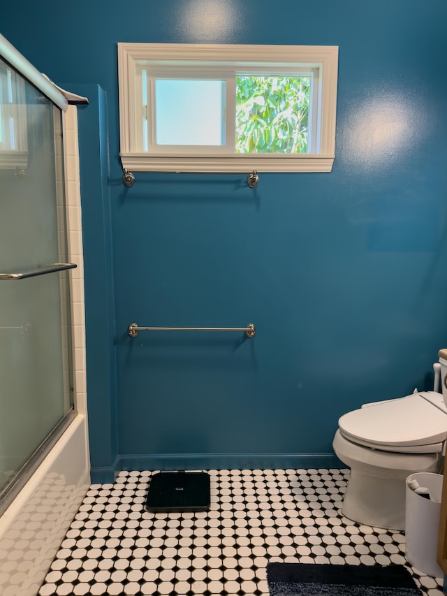 bathroom featuring enclosed tub / shower combo, baseboards, a healthy amount of sunlight, and toilet