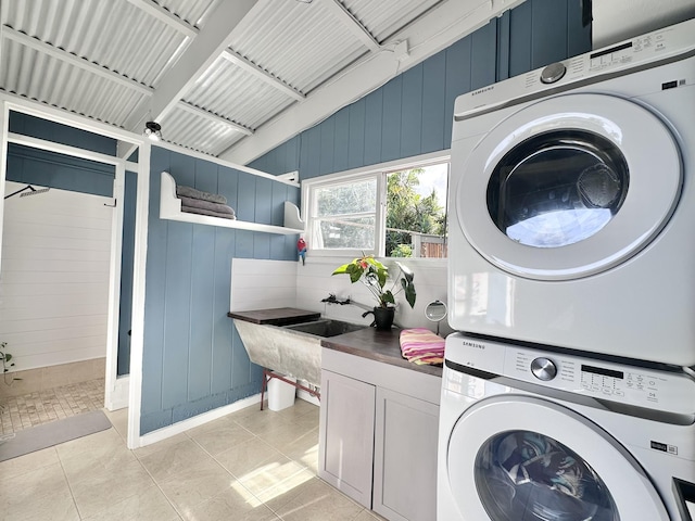 clothes washing area with light tile patterned floors, cabinet space, and stacked washing maching and dryer