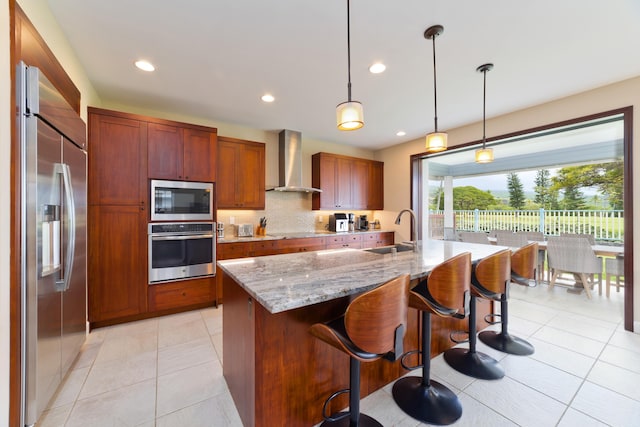 kitchen with light tile patterned floors, a sink, built in appliances, light stone countertops, and wall chimney range hood