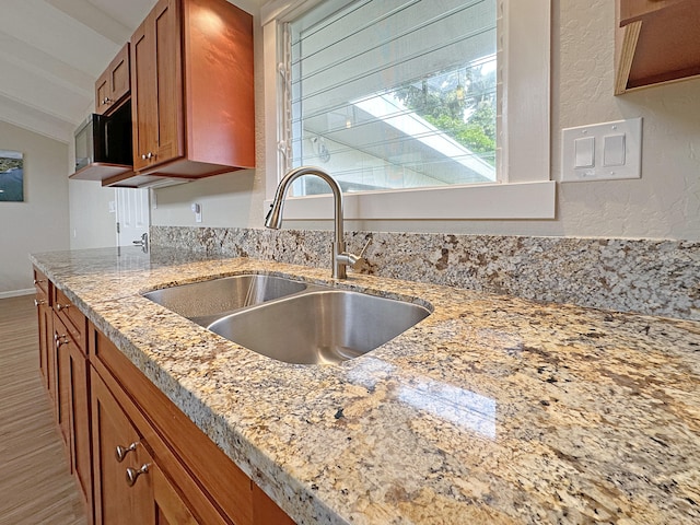 kitchen with light wood finished floors, light stone countertops, lofted ceiling, brown cabinetry, and a sink