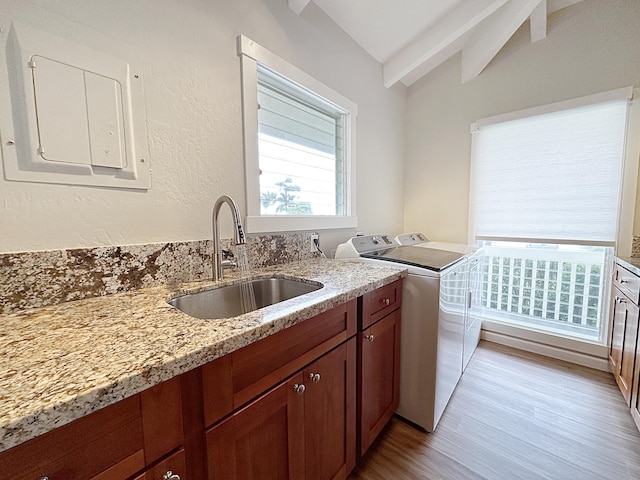 kitchen featuring light stone counters, washing machine and clothes dryer, lofted ceiling, electric panel, and a sink