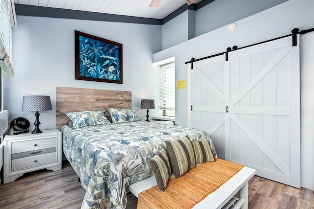 bedroom with a barn door, wood finished floors, and vaulted ceiling