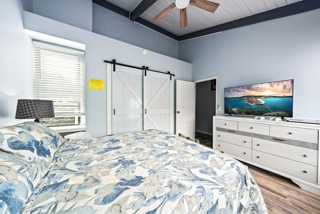 bedroom featuring beam ceiling, a ceiling fan, a barn door, and wood finished floors