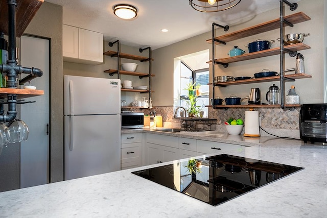 kitchen featuring open shelves, stainless steel microwave, freestanding refrigerator, and a sink