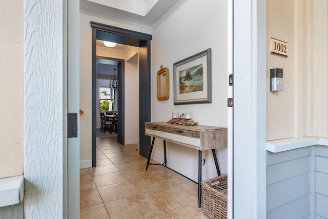 hallway with light tile patterned floors, crown molding, and baseboards