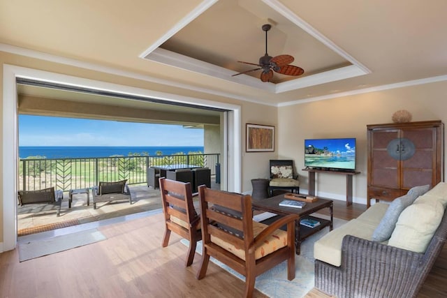 living room featuring a raised ceiling, ornamental molding, ceiling fan, wood finished floors, and baseboards