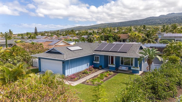 ranch-style home featuring a garage, fence, roof mounted solar panels, a mountain view, and a front yard