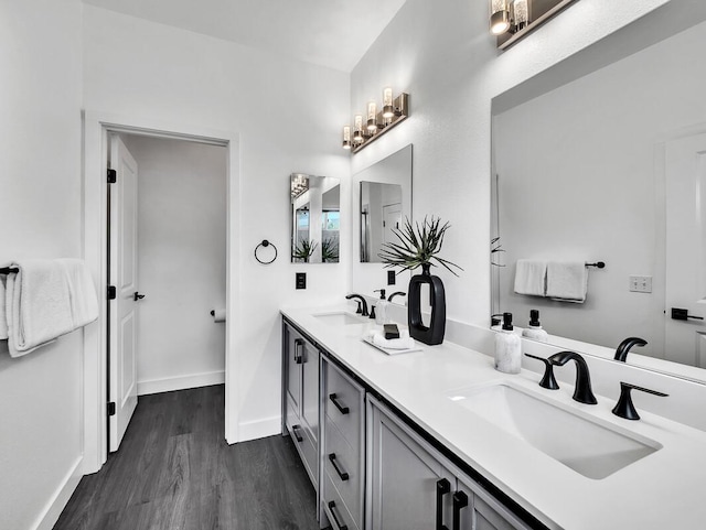 full bath with double vanity, a sink, baseboards, and wood finished floors