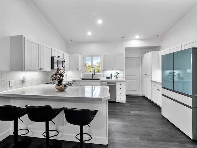 kitchen featuring white cabinets, appliances with stainless steel finishes, a breakfast bar, a peninsula, and a sink