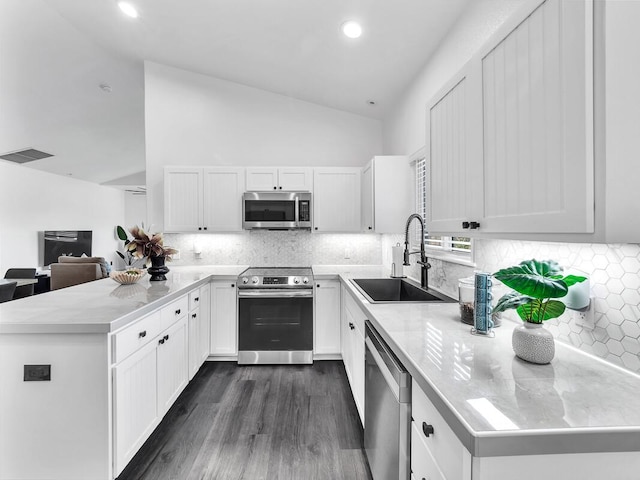 kitchen with stainless steel appliances, a peninsula, a sink, visible vents, and vaulted ceiling