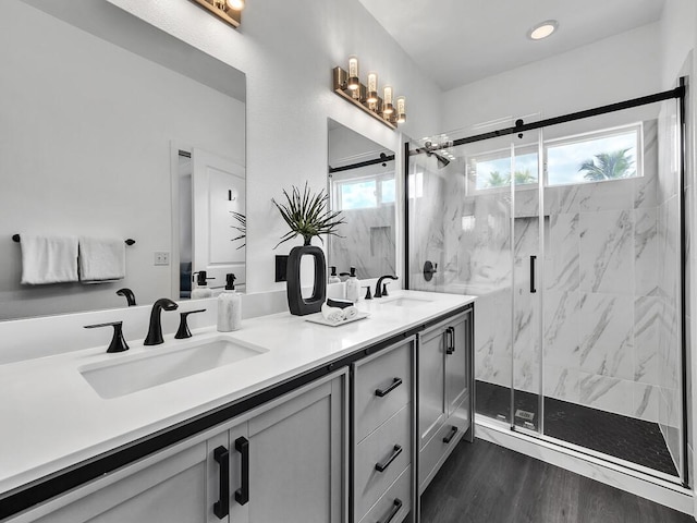 bathroom with double vanity, wood finished floors, a sink, and a marble finish shower